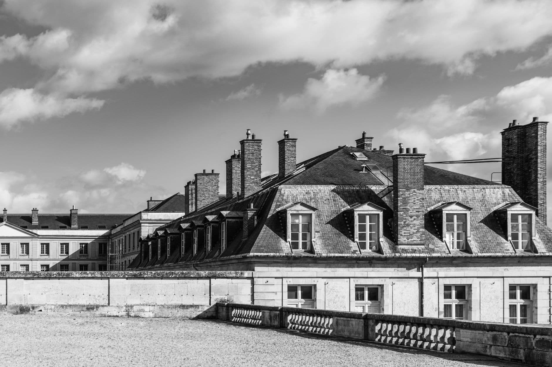 Black and white photo of classic Parisian rooftops with chimneys and dramatic clouds.
